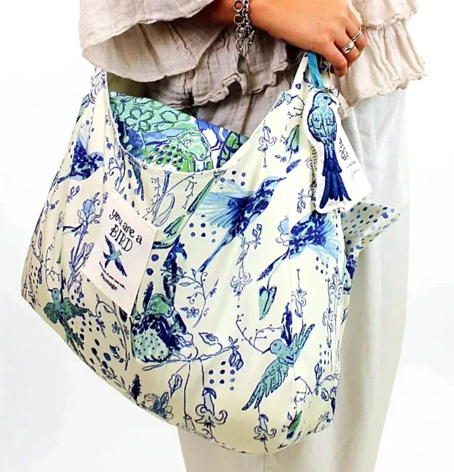 The Plumage bed-in-a-bag tote carried on the arm, with its ‘You are a BIRD’ label, embroidered bird keychain and tag