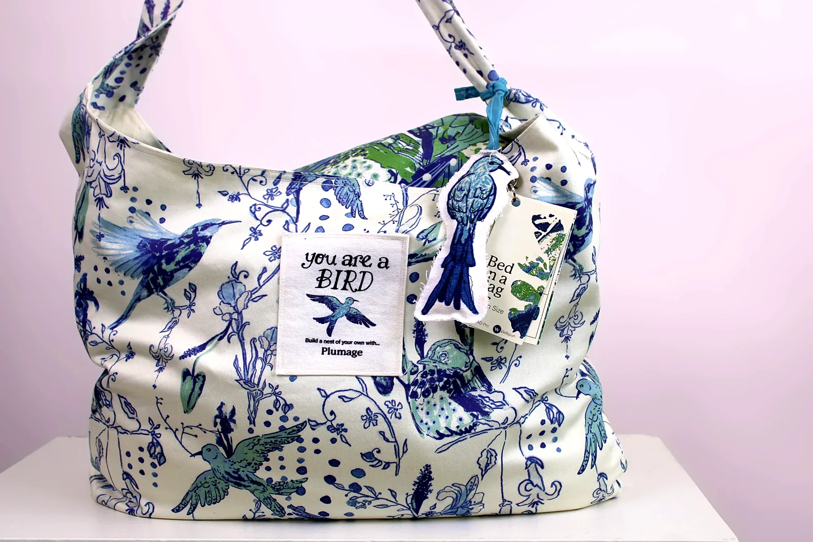 The Plumage bed-in-a-bag tote with its label, bird keychain and Bed in a Bag tag